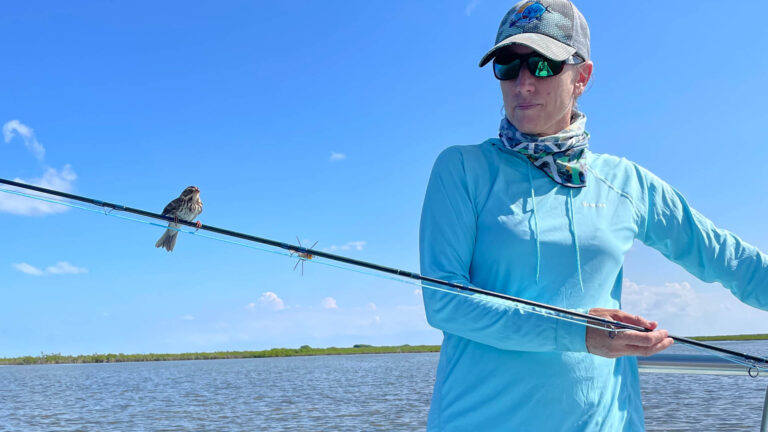 A fly fishermen has a bird perched on her rod.